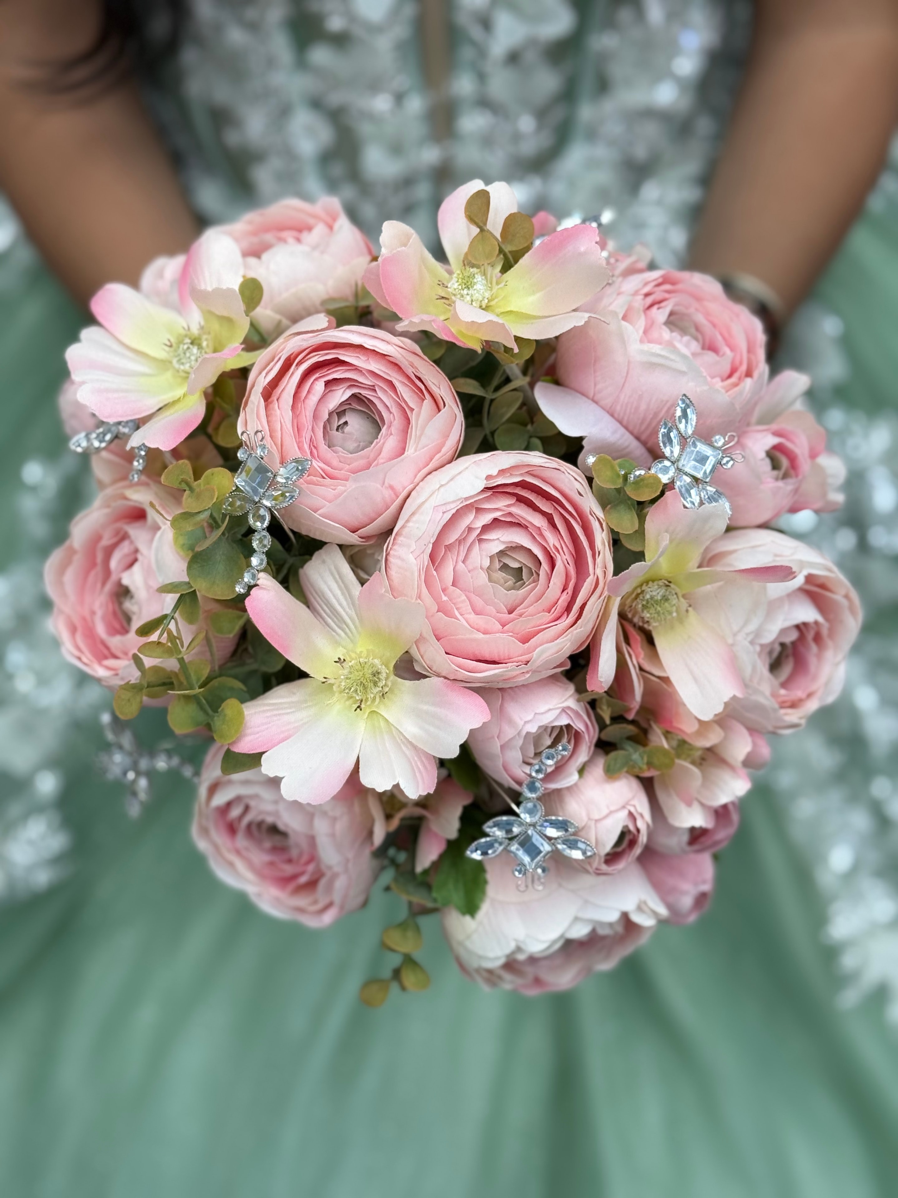 Quinceañera bouquet of pink ranunculus with crystal dragonfly jewel pins against a mint gown
