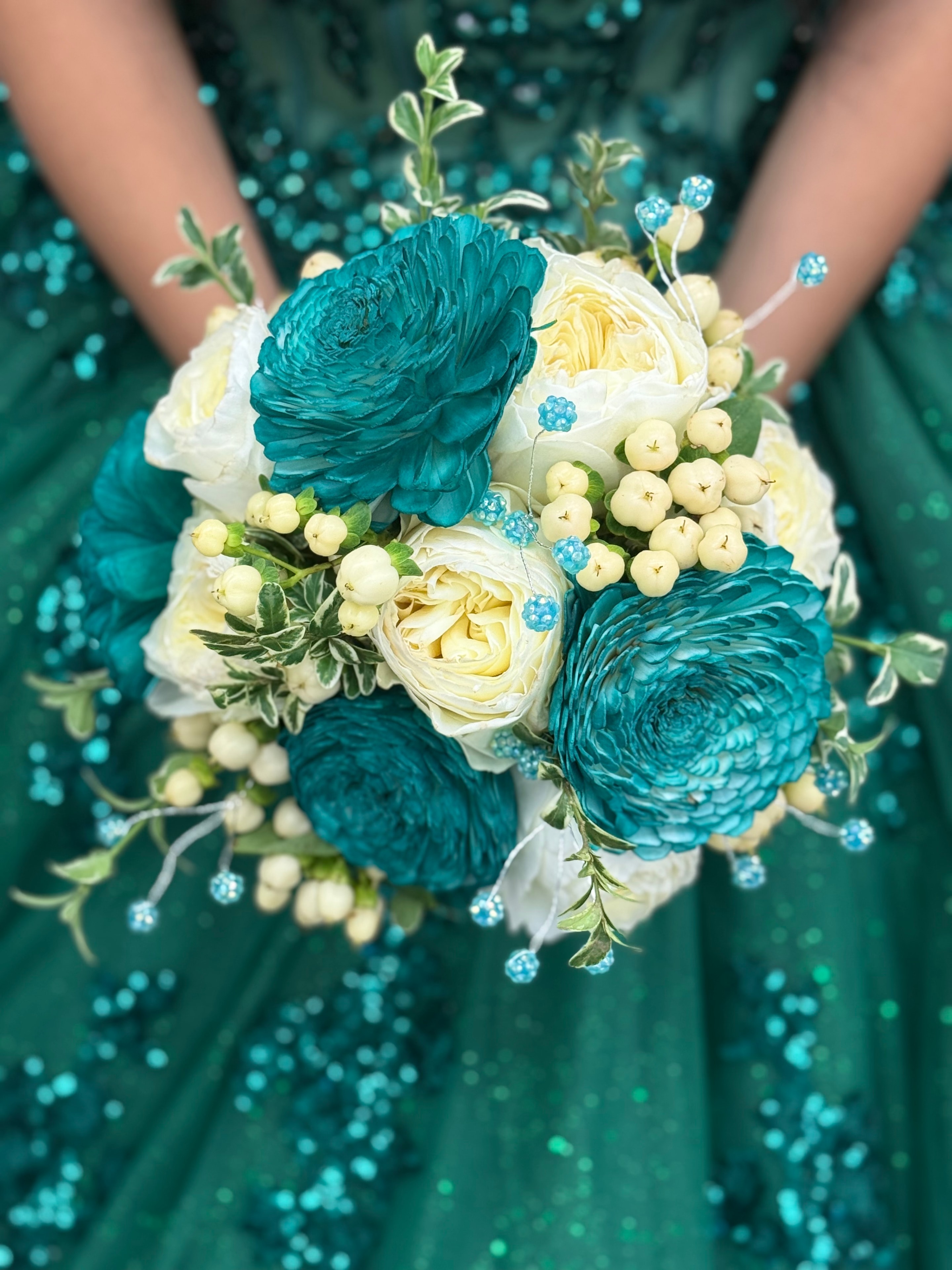 Quinceañera bouquet with teal ranunculus and cream roses against a teal sequin gown
